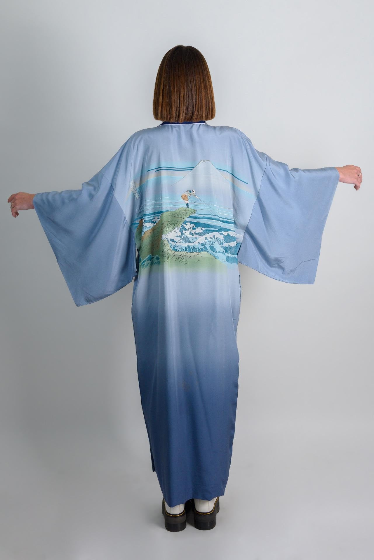 May include: A blue silk kimono with a mountain and ocean scene printed on the back. The kimono has a gradient color from light blue to dark blue.