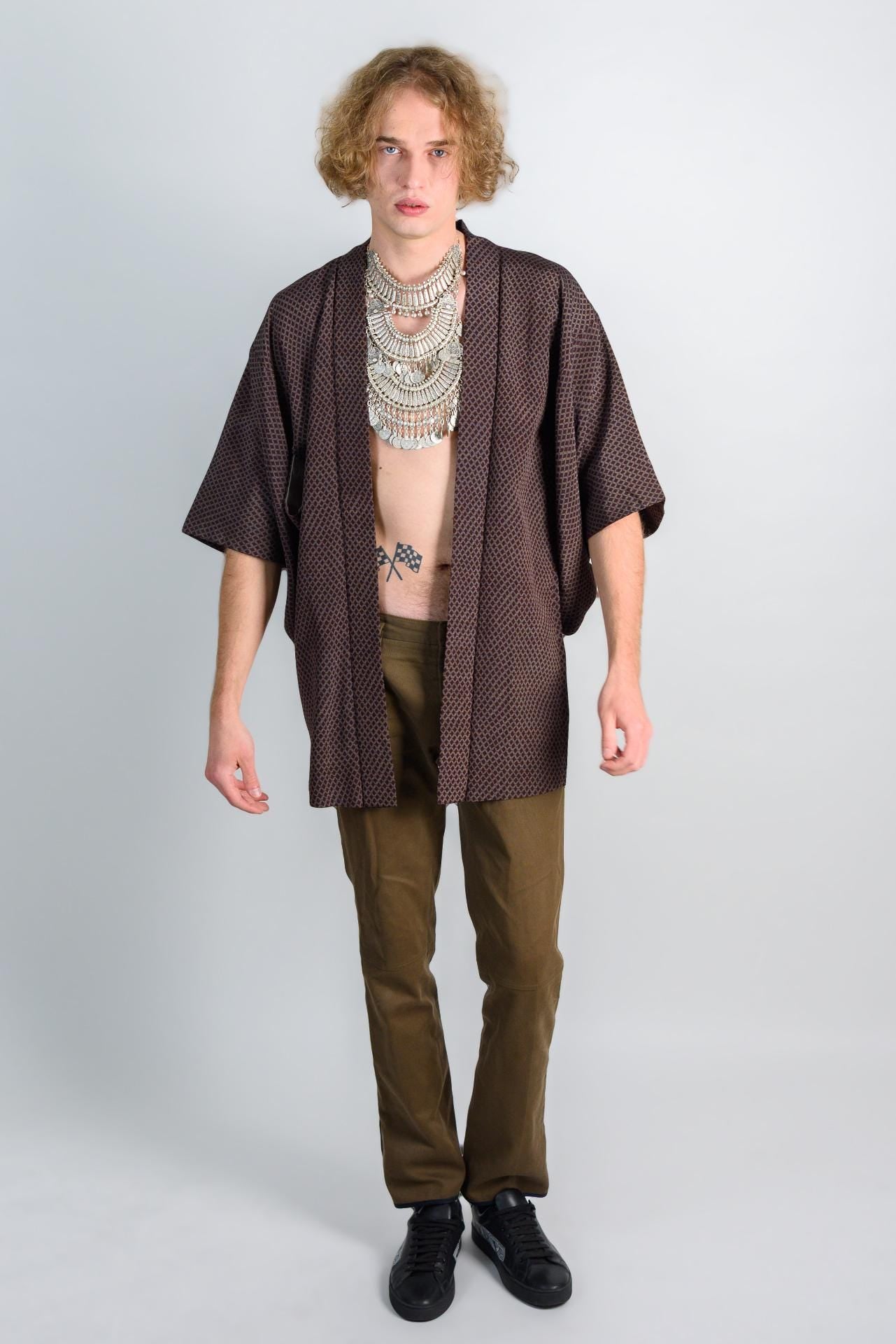 May include: A brown and black patterned kimono with a silver necklace. The person is wearing brown pants and black shoes.