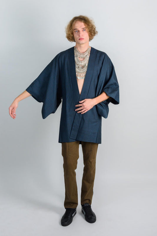 May include: A person wearing a dark blue kimono with a silver necklace and brown pants.