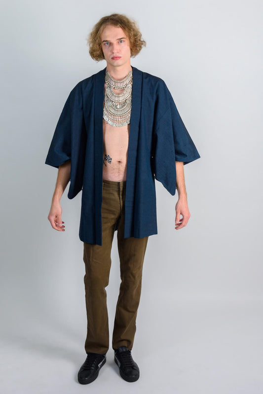 May include: A person wearing a dark blue kimono with a silver necklace and brown pants.