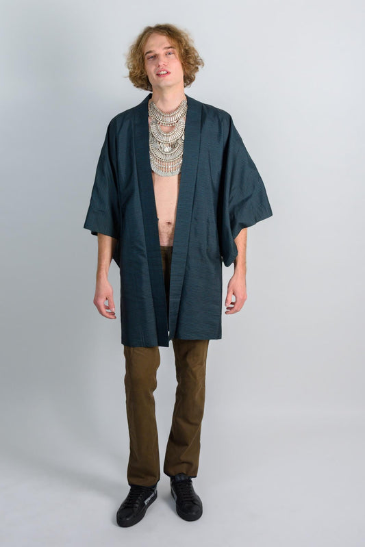 May include: A dark green kimono with a long sleeve and a simple design. The kimono is worn over brown pants and black shoes.