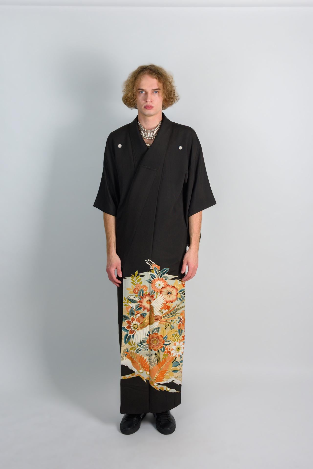 May include: A black kimono with a floral pattern on the bottom half. The kimono has a v-neck and is worn with a silver necklace.