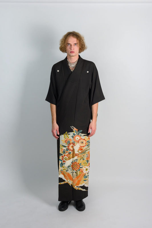 May include: A black kimono with a floral pattern on the bottom half. The kimono has a v-neck and is worn with a silver necklace.