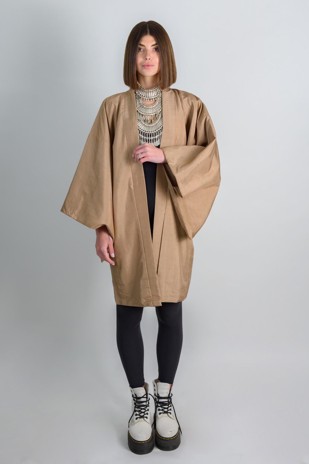 May include: A tan kimono with long sleeves and a black shirt underneath. The person is wearing black leggings and white boots.