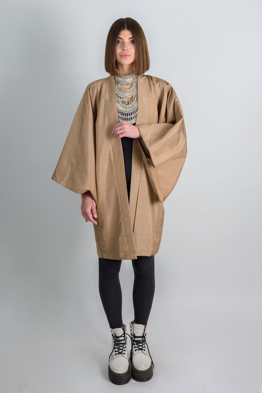 May include: A tan kimono with long sleeves and a black shirt underneath. The person is wearing black leggings and white boots.