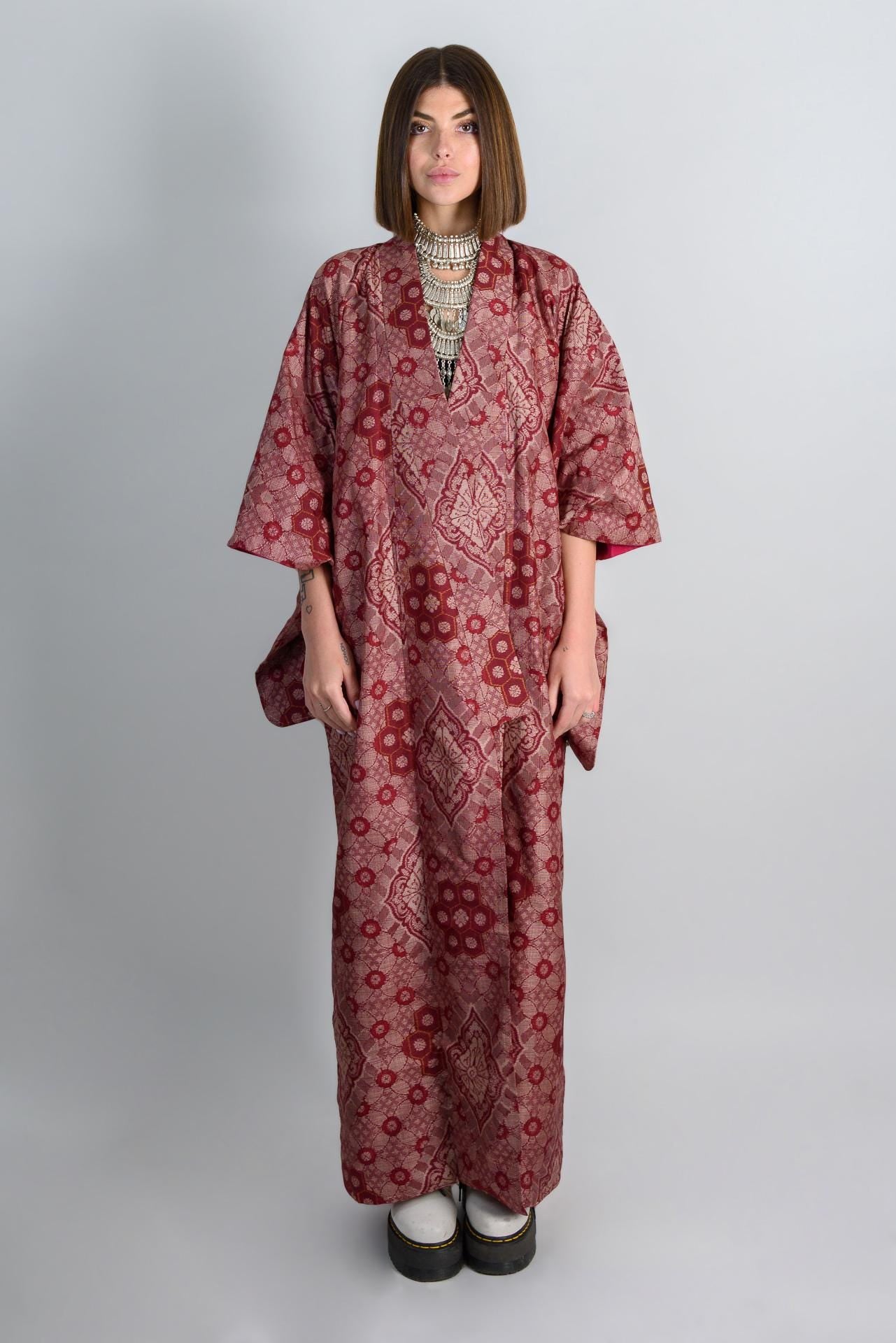 May include: A long, red and pink patterned robe with a V-neckline. The robe has a loose fit and is made of a silky fabric.