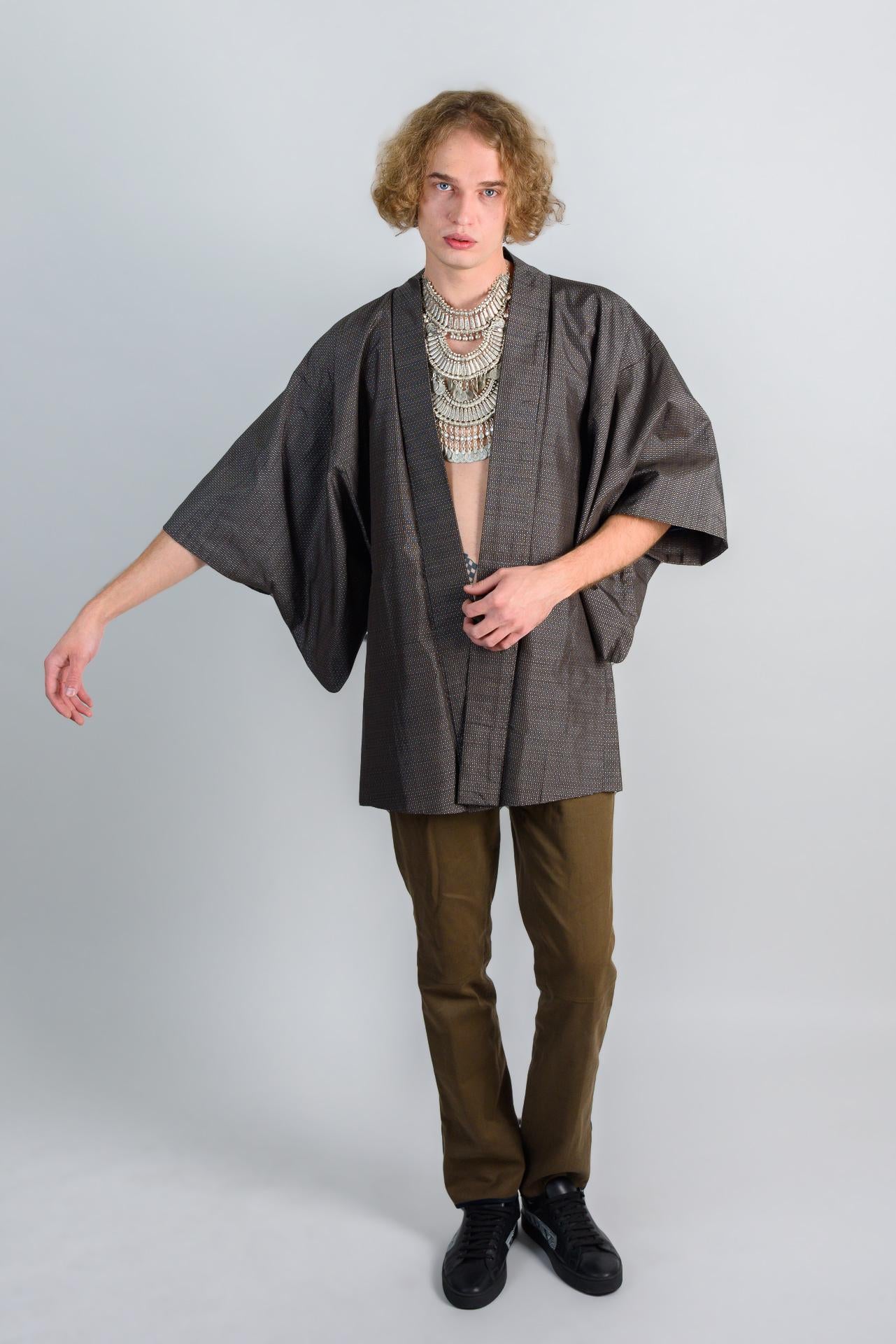 May include: A person wearing a dark gray kimono with a silver necklace and brown pants.