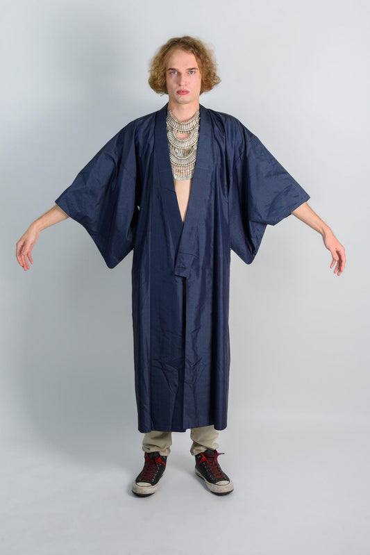 May include: A person wearing a dark blue kimono with a silver necklace and black and red sneakers.