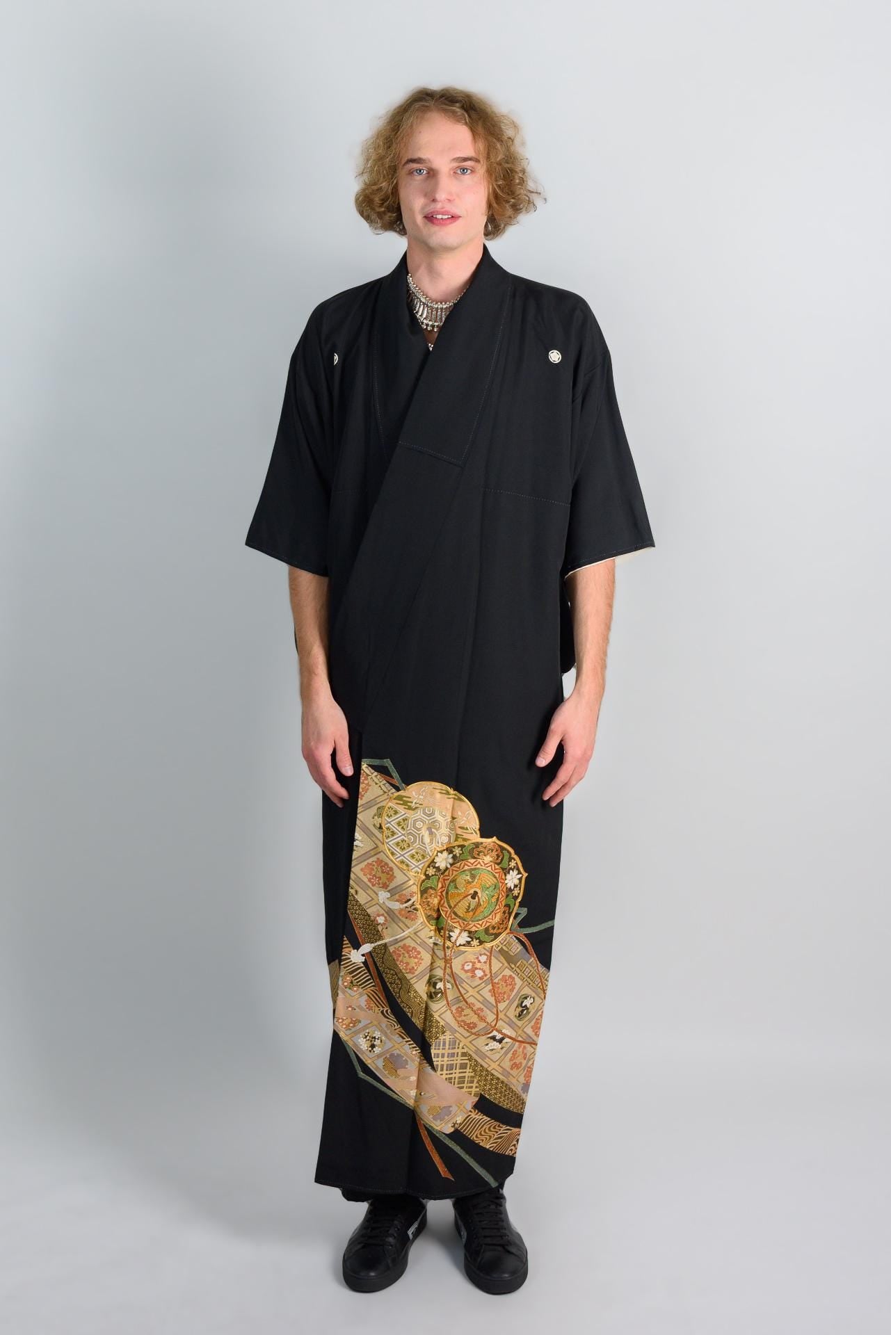 May include: A black kimono with a gold and green patterned design on the bottom half of the garment.