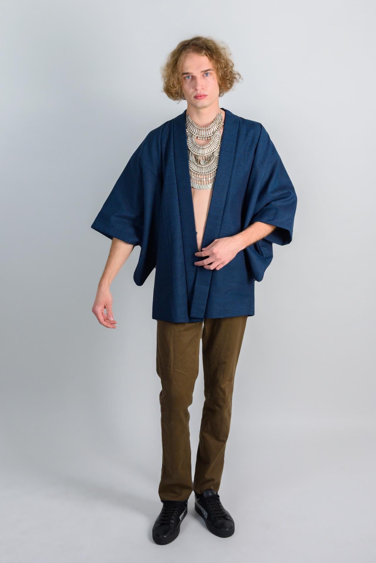 May include: A person wearing a dark blue kimono with a silver necklace and brown pants.