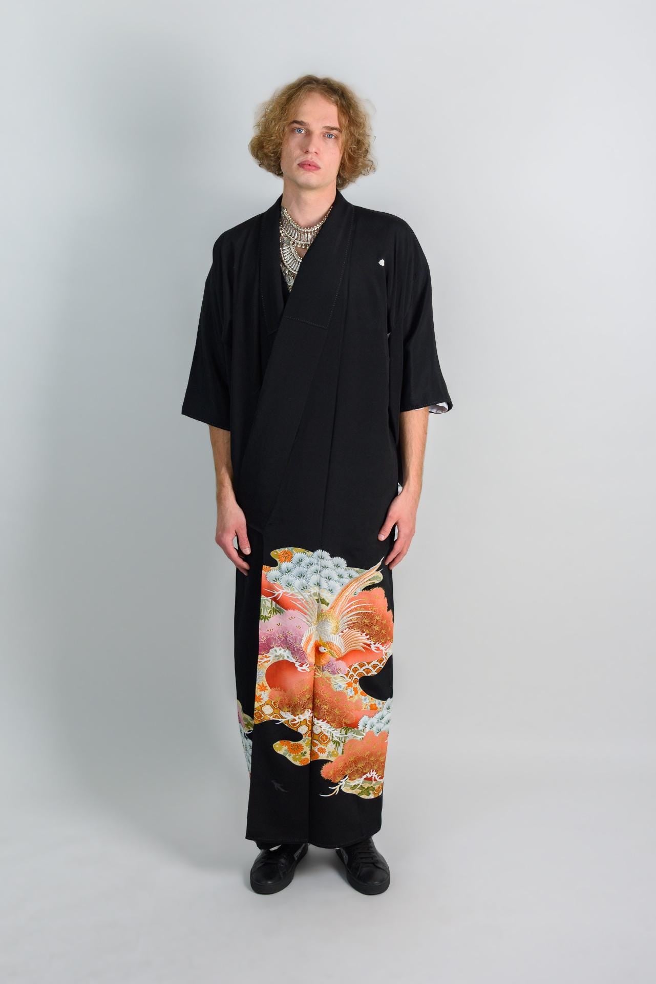 May include: A person wearing a black kimono with a colorful floral pattern on the bottom half. The kimono has a simple design and is made of a soft, flowing fabric.