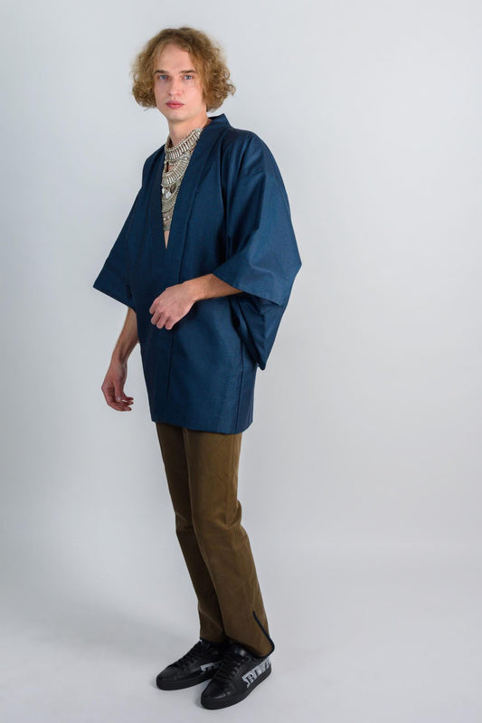 May include: A person wearing a dark blue kimono with a silver necklace and brown pants. The person is wearing black shoes with white lettering.