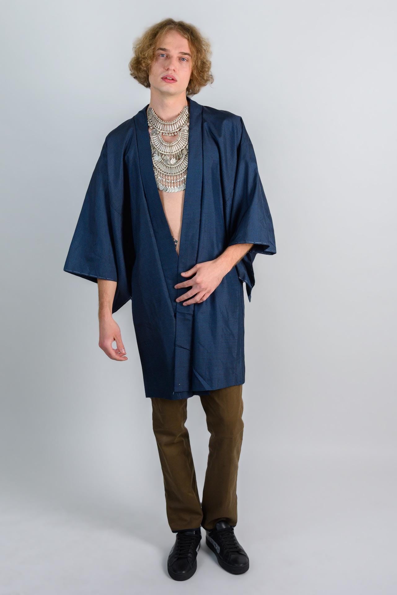 May include: A person wearing a dark blue kimono with a silver necklace and brown pants.