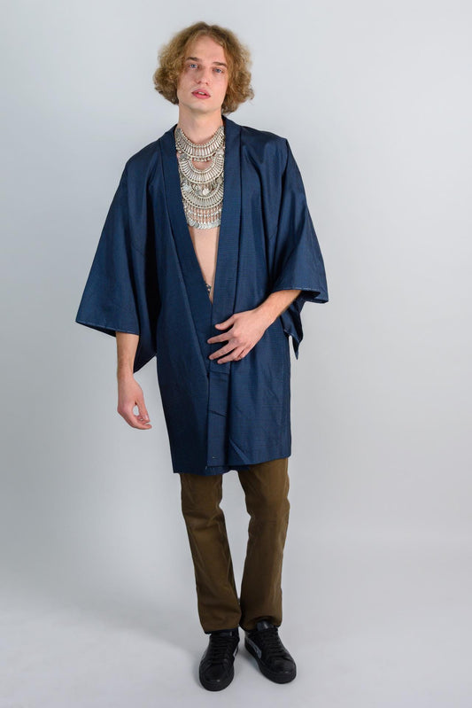 May include: A person wearing a dark blue kimono with a silver necklace and brown pants.