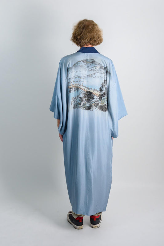 May include: A light blue kimono with a printed design of a bridge and mountains. The kimono has a navy blue collar.